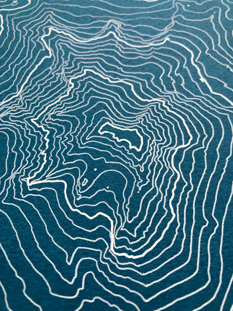 Framed pen-plotted topographic map in the blue colorway displayed in a real room, from the same series as this topographic map of Borah Peak, Idaho