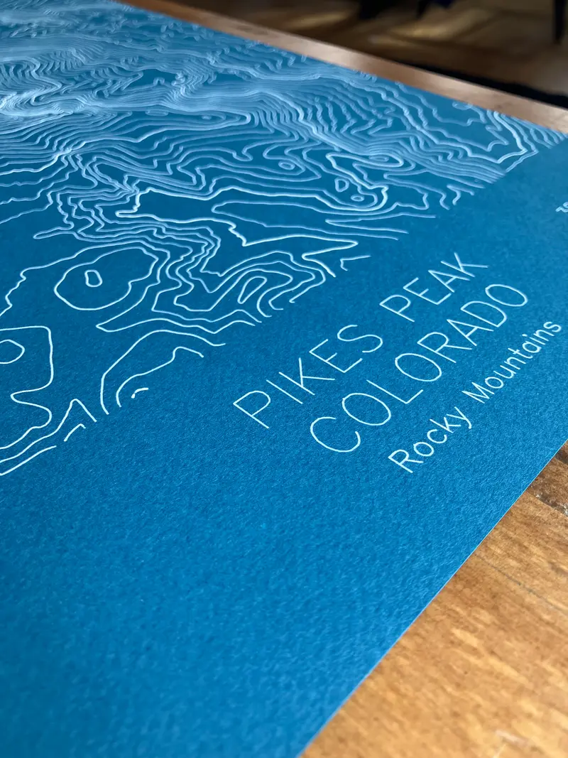 Framed pen-plotted topographic map in the blue colorway displayed in a real room, from the same series as this topographic map of Borah Peak, Idaho
